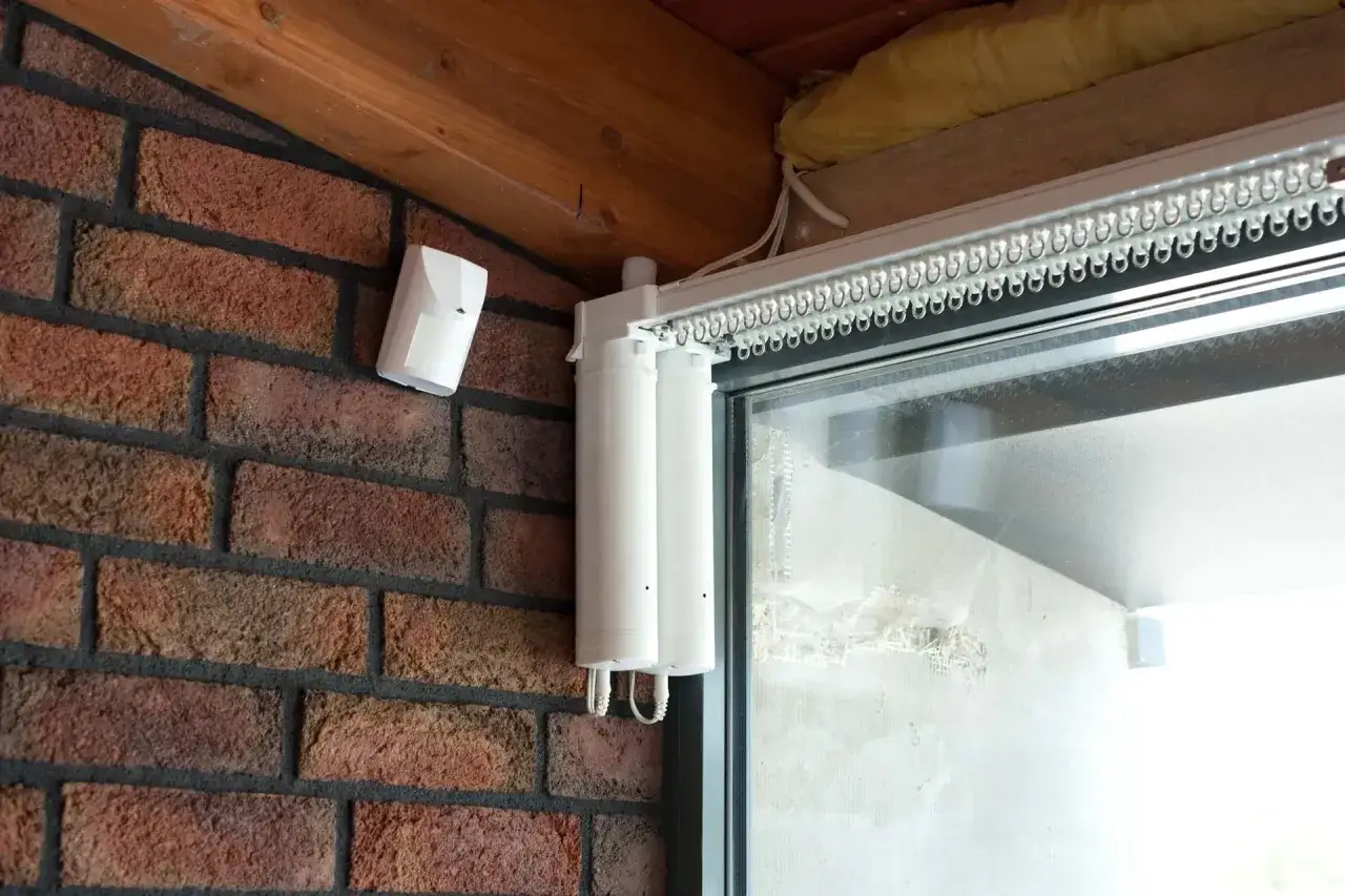 System elektryczne zasłony wewnętrzne z napędem i czujnikiem ruchu na ceglanej ścianie.