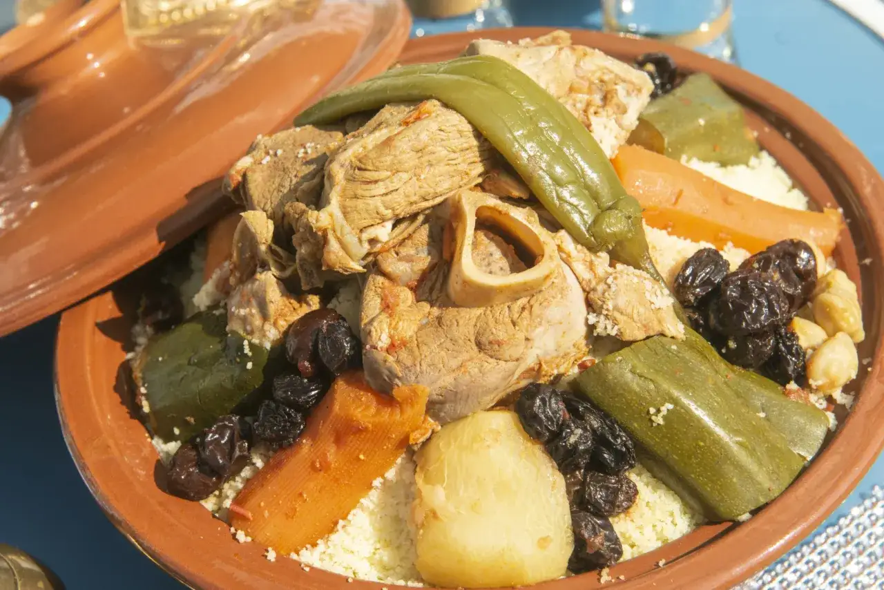Un plat de couscous alg&eacute;rien g&eacute;n&eacute;reux avec viande, l&eacute;gumes et raisins secs, servi dans un plat en terre cuite.