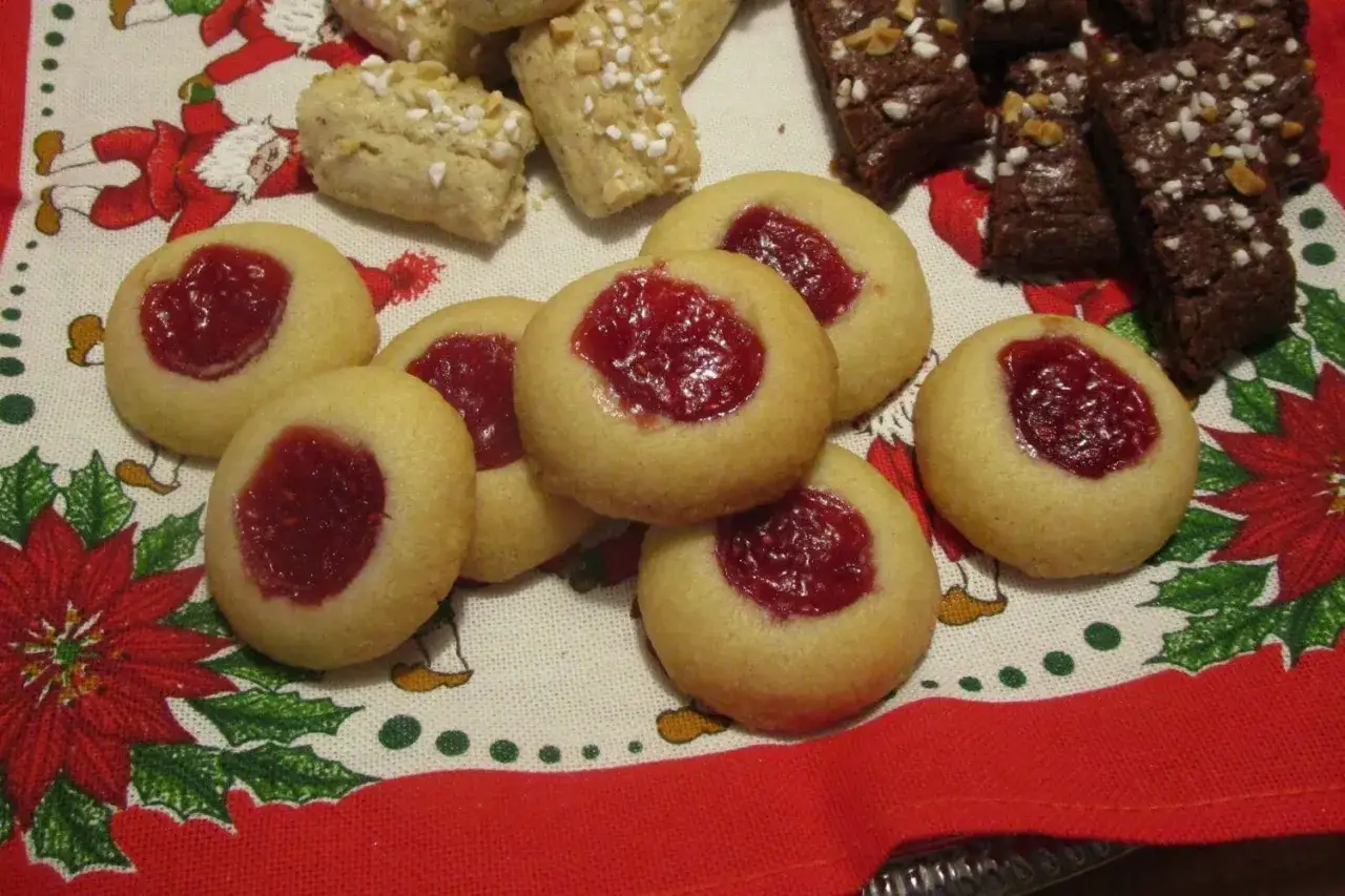 Hallongrottor recept: små, runda kakor med hallonsylt i mitten, bredvid chokladkakor och nötter på en julduk.