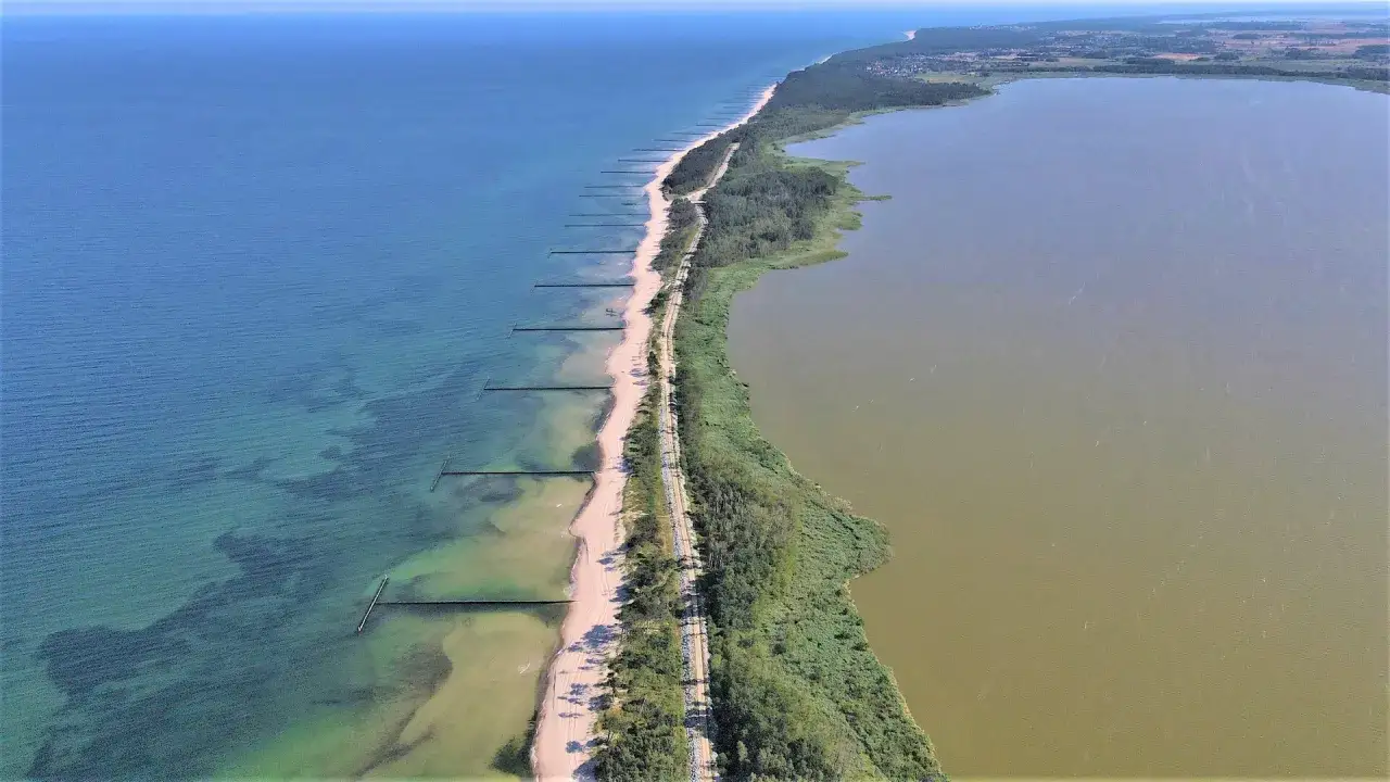 Piękne wicie jezioro i morze rozdzielone piaszczystą plażą i lasem. Woda w jeziorze jest mętna, a w morzu przejrzysta.