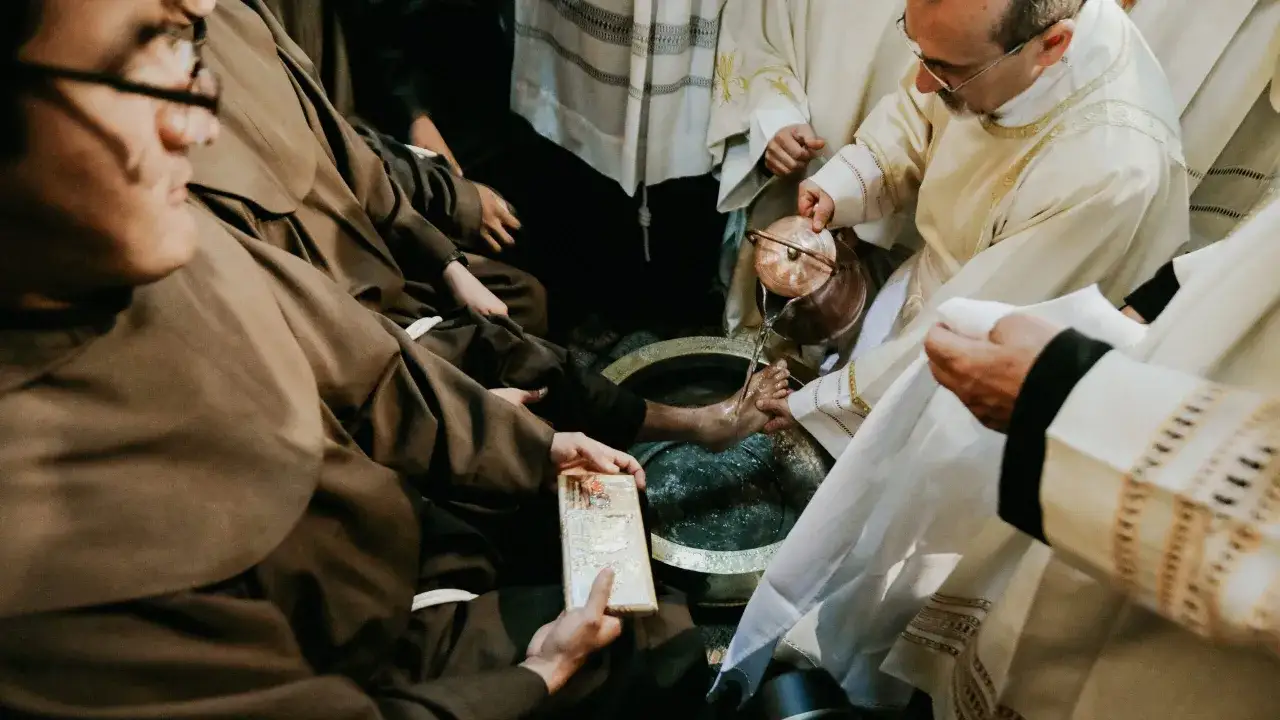 During a holy Thursday Catholic homily, a priest washes the feet of a man in a basin, symbolizing Christ's humility.
