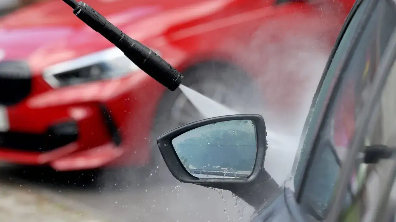 Hochdruckreiniger sprüht Wasser auf den Seitenspiegel eines Autos. Vorsicht vor Kratzern durch Waschanlage!