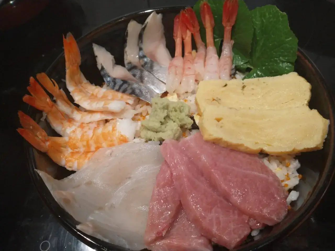 Miseczka sushi z krewetkami, rybą, omletem i zieloną pastą, która wygląda jak sos wasabi.