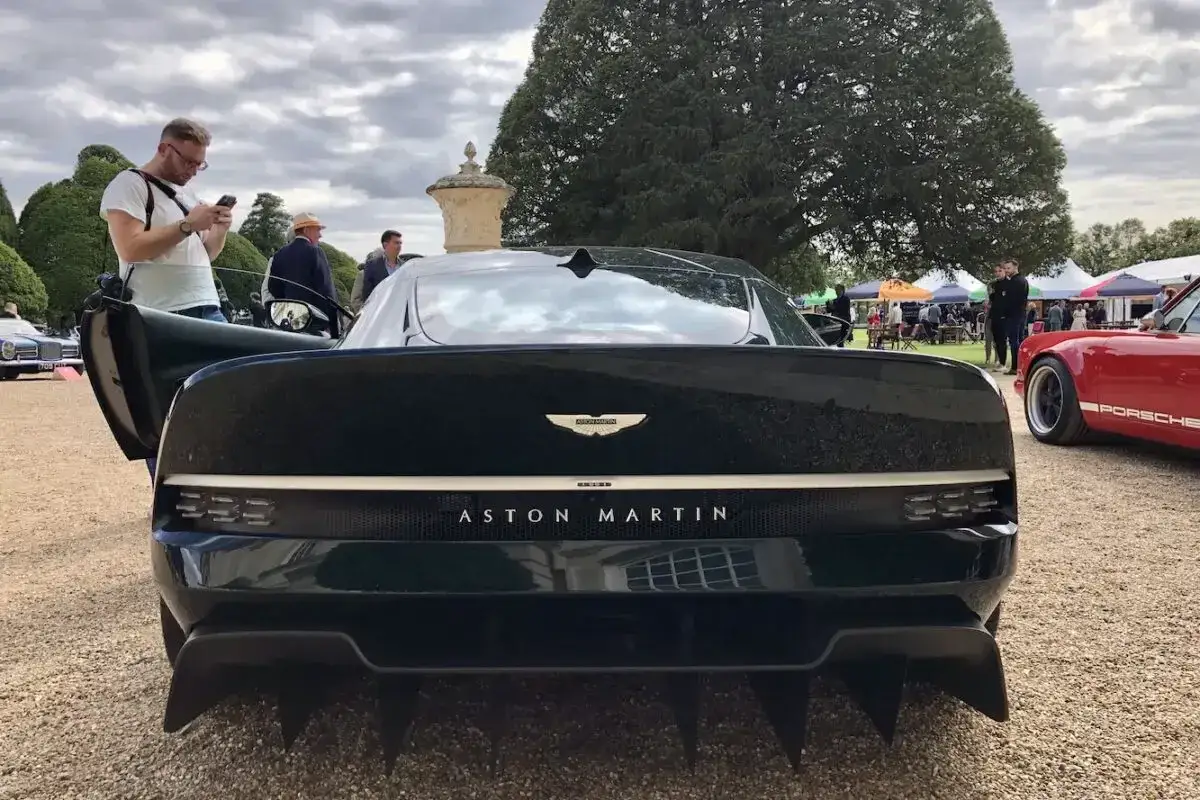 Tylna część czarnego Aston Martin Victor z otwartymi drzwiami, obok czerwonego Porsche.