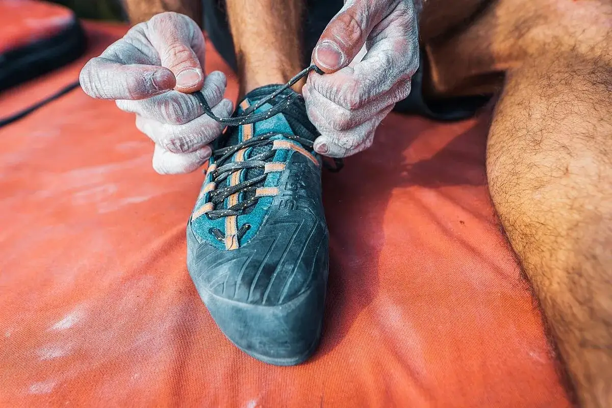 Hände mit Magnesia binden Kletterschuh. Die richtigen Schuhe für den Klettersteig sind entscheidend für Halt und Komfort.