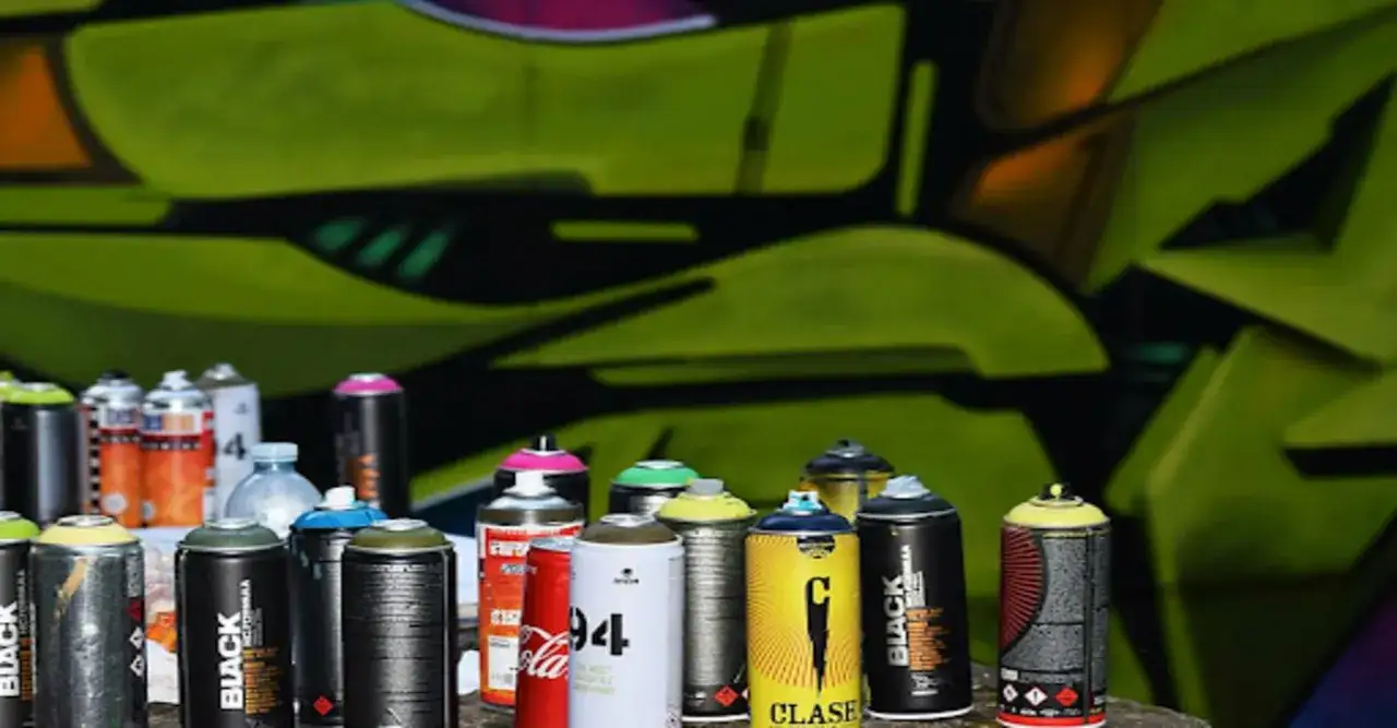 Szeroki wybór puszek z farbą w sprayu, gotowych do tworzenia dzieł sztuki. W tle zielone graffiti, sugerujące potencjalną emisję LZO.