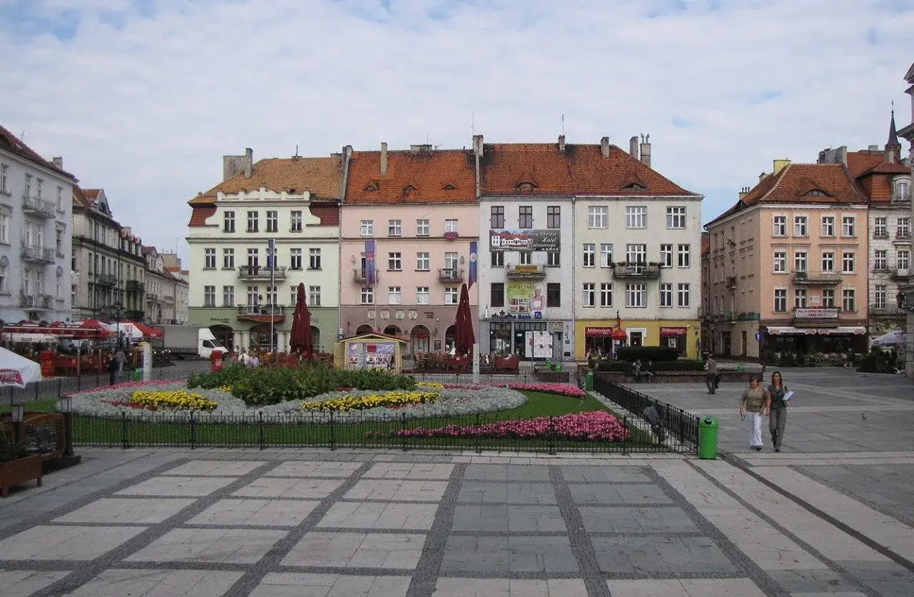 Rynek w Kaliszu, najstarszym mieście w Polsce, z kolorowymi kamienicami i kwitnącym skwerem.