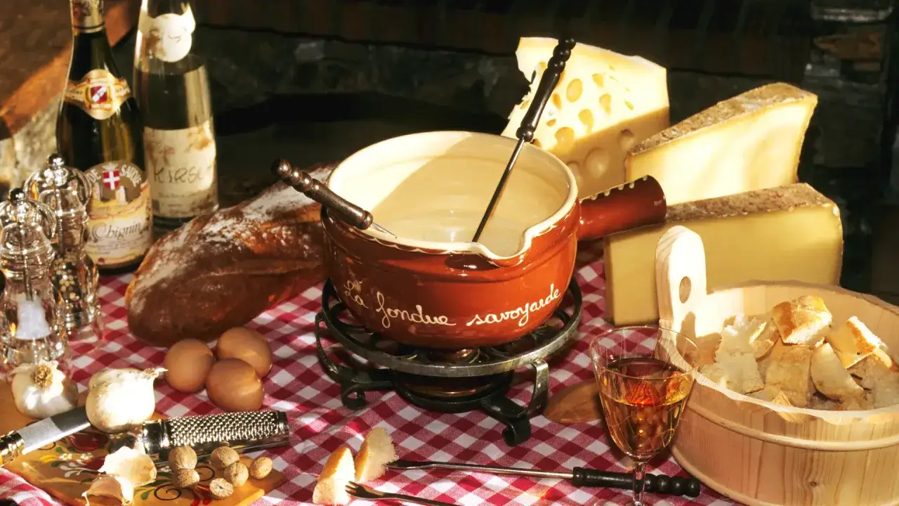 Un plat savoyard r&eacute;confortant : fondue au fromage, pain, vin blanc et ingr&eacute;dients frais sur une nappe &agrave; carreaux rouges.
