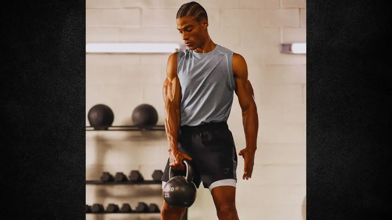 Man i grått linne och svarta shorts håller en kettlebell redo för en kb snatch.