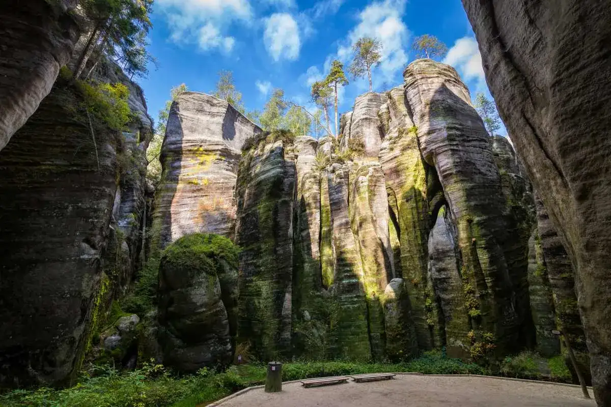 Skalny labirynt, idealny na wycieczki jednodniowe z Wrocławia. Zielony mech porasta wysokie, strzeliste skały, a niebo błękitnieje nad nimi.
