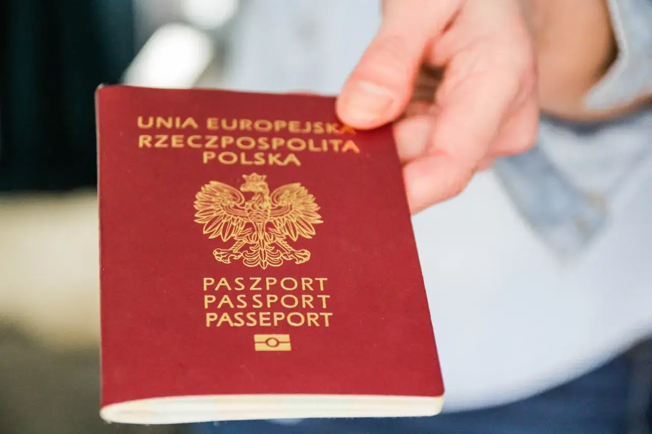 Dłoń trzyma polski paszport. Numer paszportu znajduje się na stronie z danymi osobowymi, która nie jest widoczna na okładce.