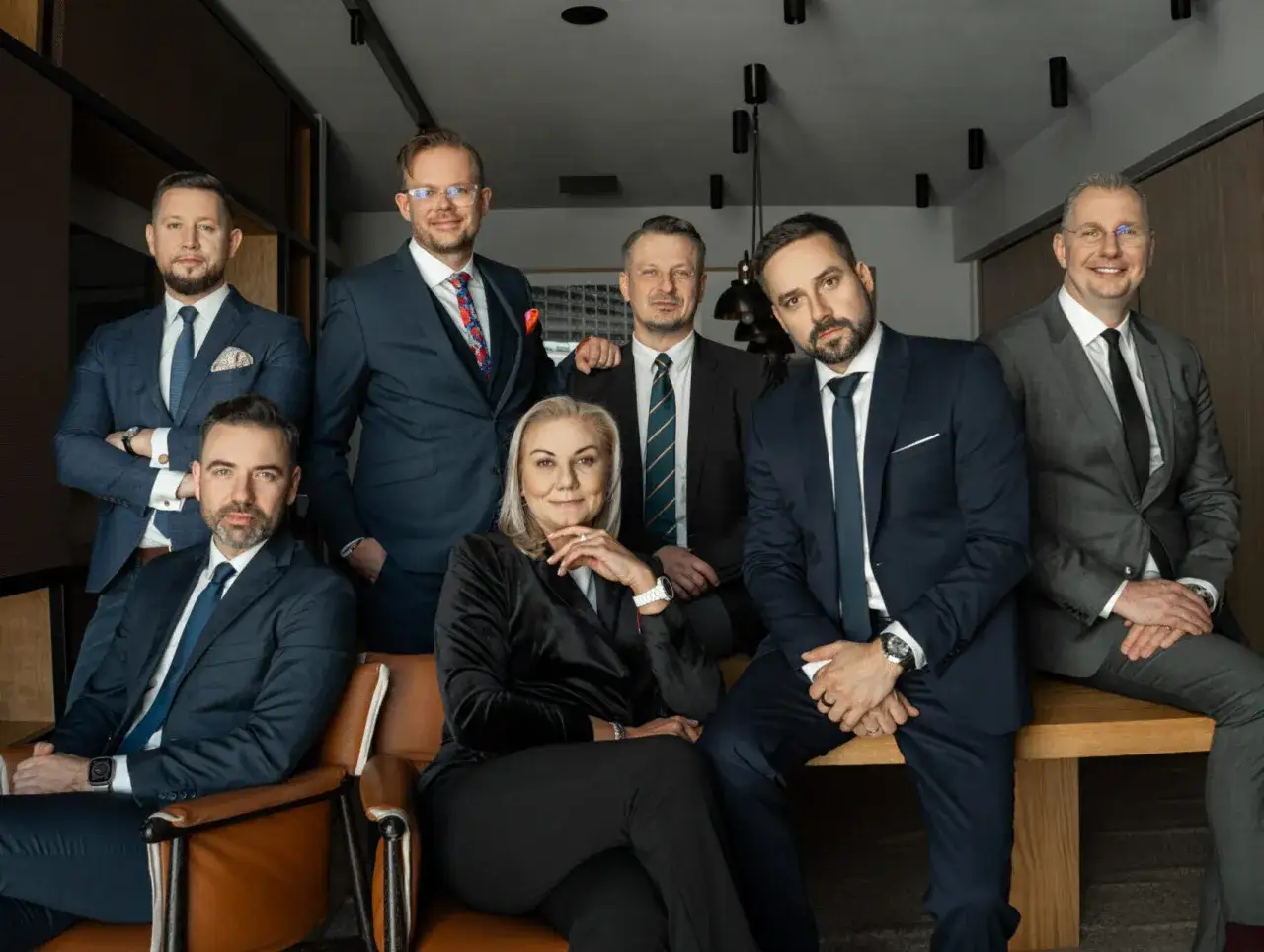 Grupa siedmiu profesjonalistów w garniturach, pozujących do zdjęcia w nowoczesnym biurze.