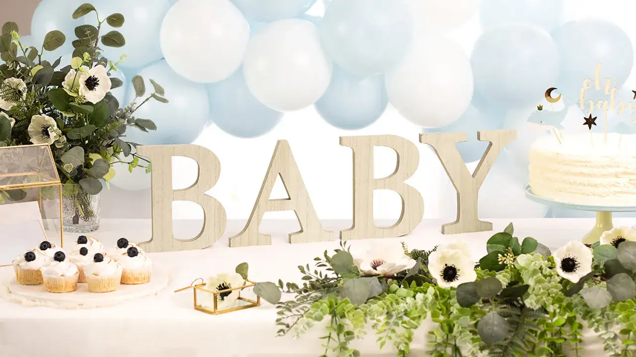Dekorationer för babyshower med bokstäverna BABY, ballonger och en tårta. Inga synliga ballongtyngder.