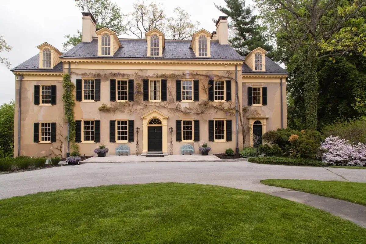 La **r&eacute;novation maison de ma&icirc;tre** a redonn&eacute; vie &agrave; cette demeure historique aux volets noirs et aux fen&ecirc;tres claires, entour&eacute;e d'un jardin verdoyant.