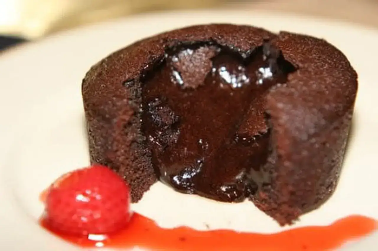 Fondant au chocolat cœur coulant, prêt à être dégusté. Une fraise et un coulis rouge accompagnent ce délice.