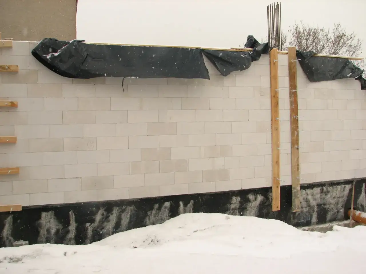 Śnieg i lód wokół świeżo murowanej ściany z bloczków. Nocne przymrozki mogą zagrozić pracom budowlanym.