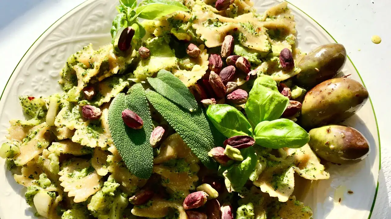 Farfalle condite con un saporito pesto di salvia, guarnite con pistacchi, basilico e olive verdi.