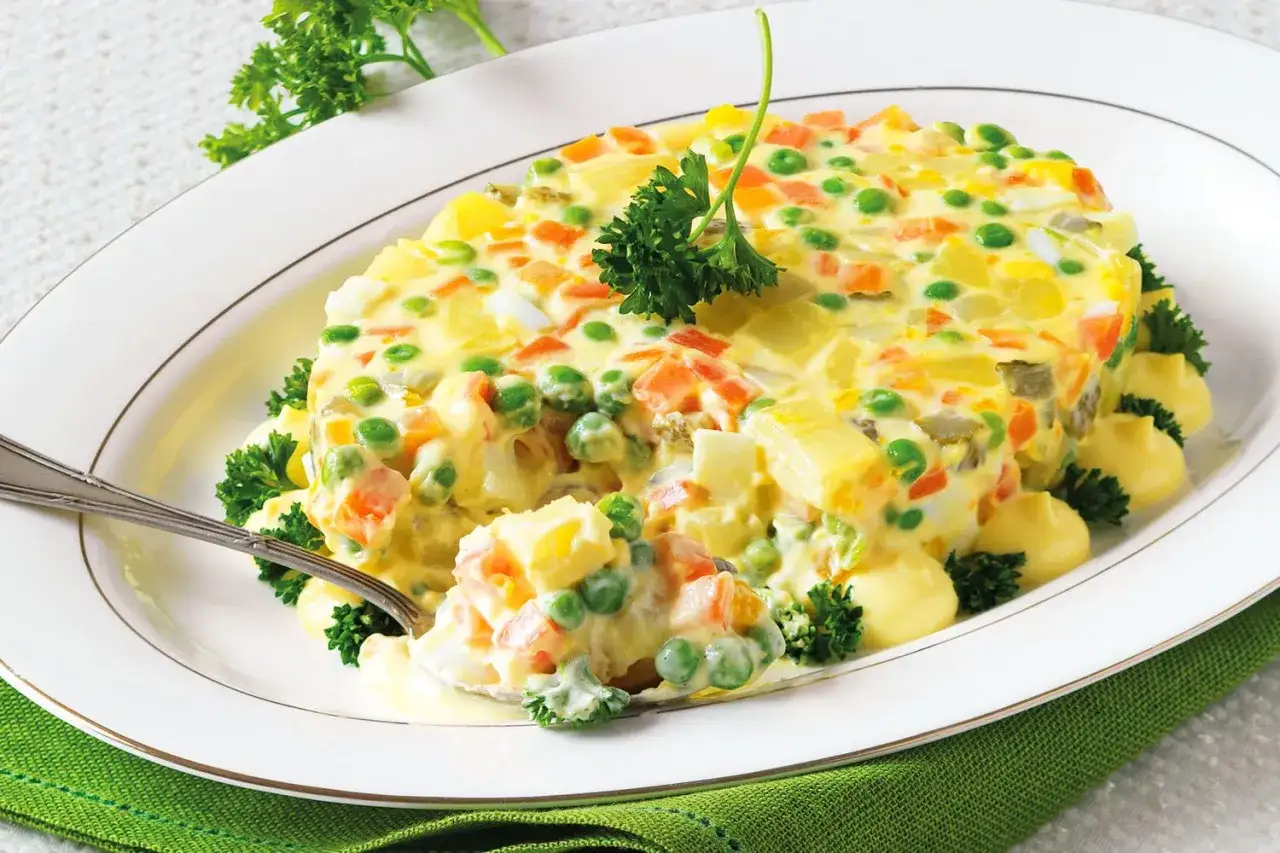 Insalata russa ricetta: un piatto cremoso con patate, carote, piselli e uova, guarnito con prezzemolo fresco.