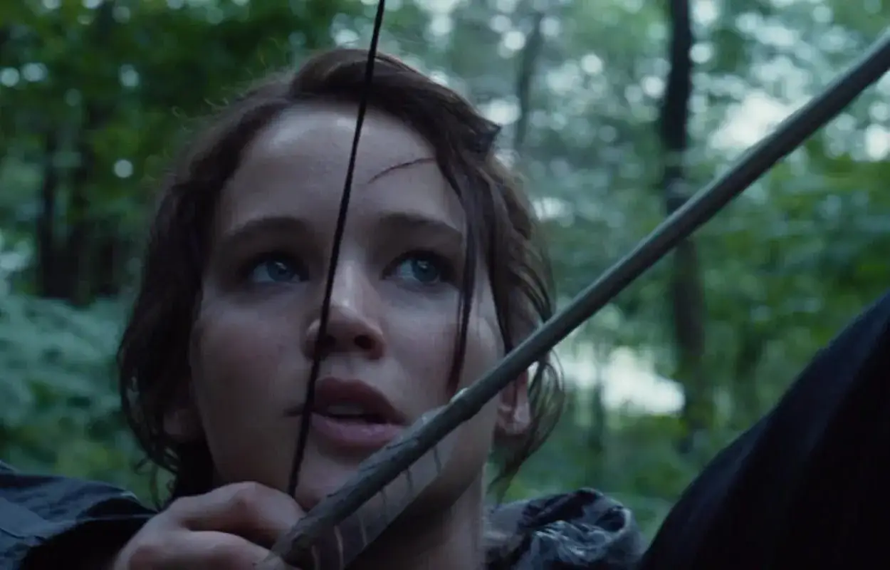 Katniss Everdeen siktar med pilbåge i skogen, redo för hunger games ordning.
