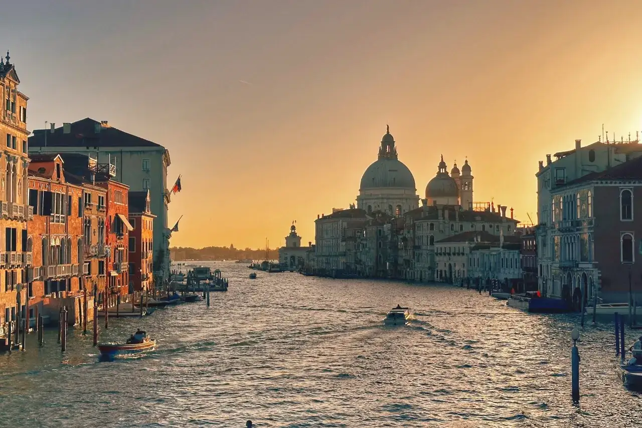 Zachód słońca nad Canal Grande w Wenecji w październiku. Woda lśni, łodzie płyną, a zabytkowe budynki otaczają kanał.