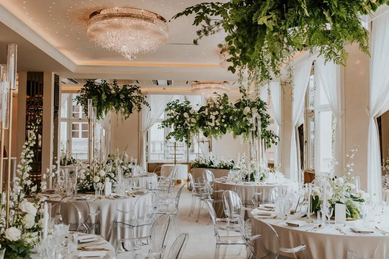 Eleganckie stoły z białymi kwiatami i kryształowymi żyrandolami tworzą atmosferę glamour wesela.
