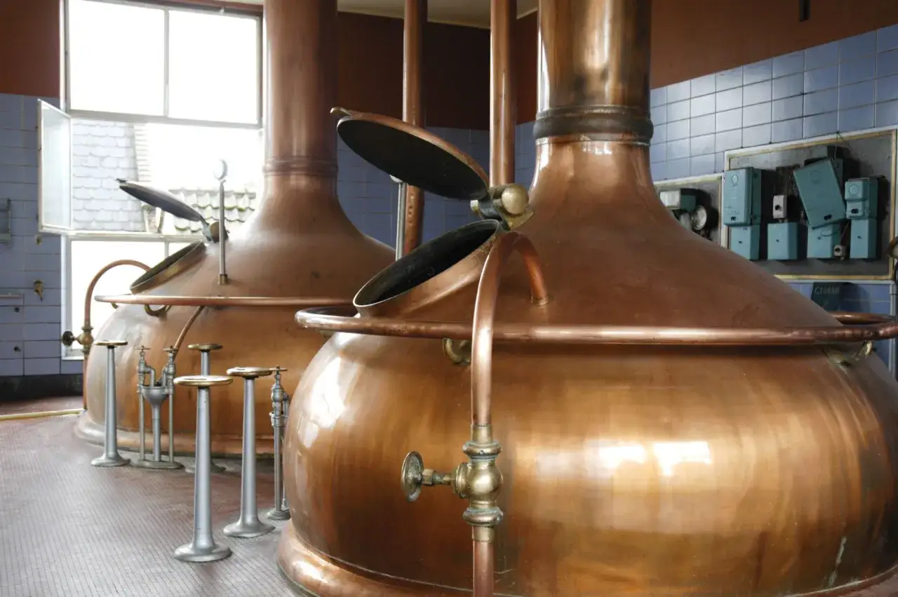 Grandi alambicchi di rame brillano nella distilleria, pronti per il processo di produzione. Het anker, simbolo di stabilit&agrave;, sembra ancorato in questo luogo di tradizione.