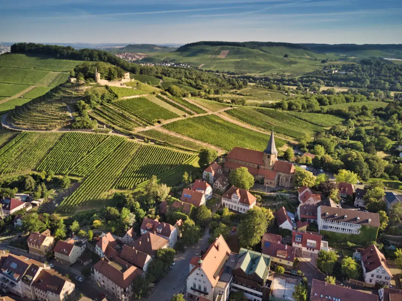 Blick über Weinberge und ein Dorf mit Kirche, ideal für eine Weinsberger Weinwanderung.