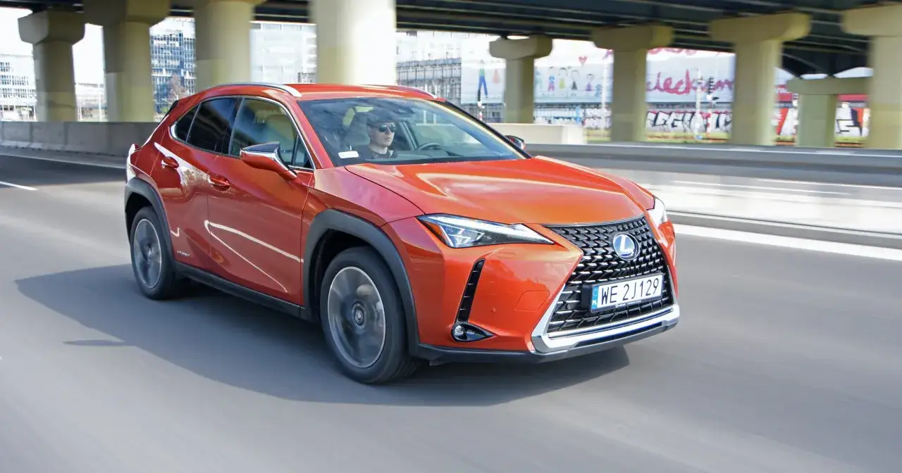 Pomarańczowy Lexus UX 250h jedzie po drodze pod wiaduktem.