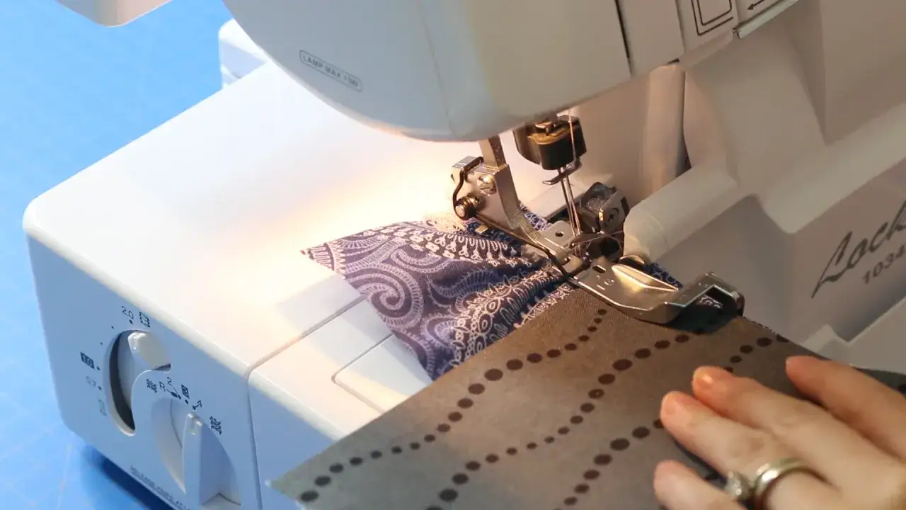 A close-up of a serger creating a gathering effect on patterned fabric.