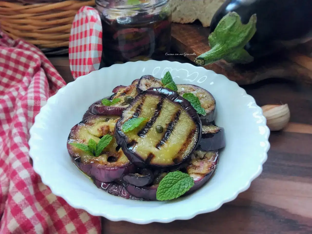 Melanzane grigliate in friggitrice ad aria, condite con olio, capperi e menta, servite in una ciotola bianca.