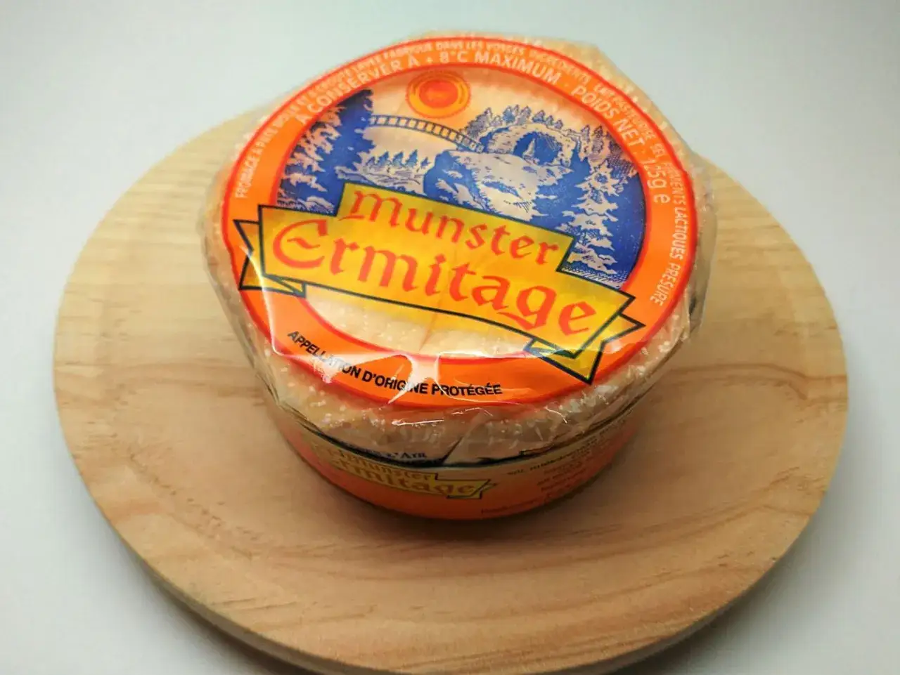 Queso Munster Ermitage, con su etiqueta naranja y azul que muestra un paisaje monta&ntilde;oso, listo para ser disfrutado.