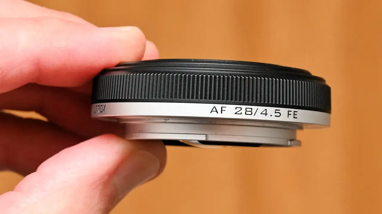 A hand holds a compact, black and silver pancake lens, labeled 