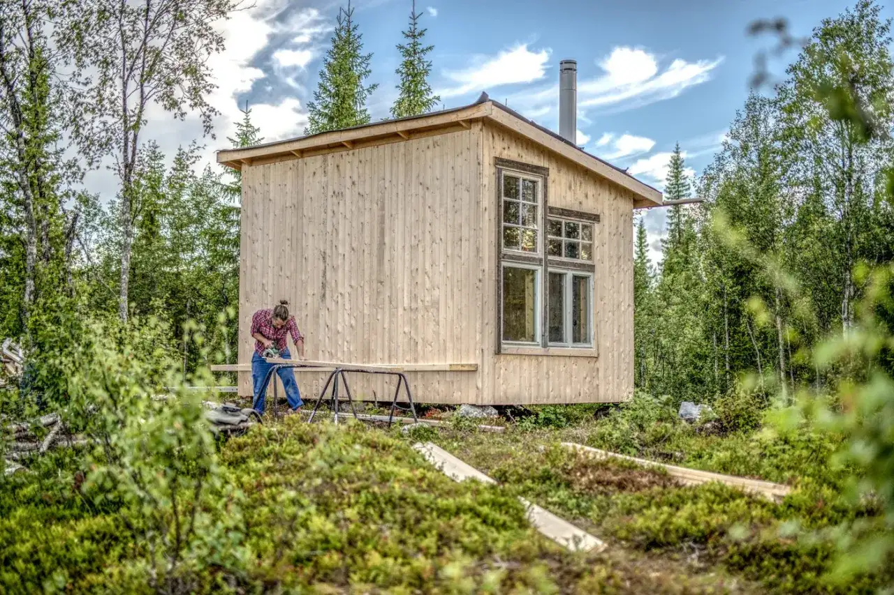 Markus Torgeby familj bygger sitt drömhus i skogen. En person sågar trä vid den nya timmerstugan.