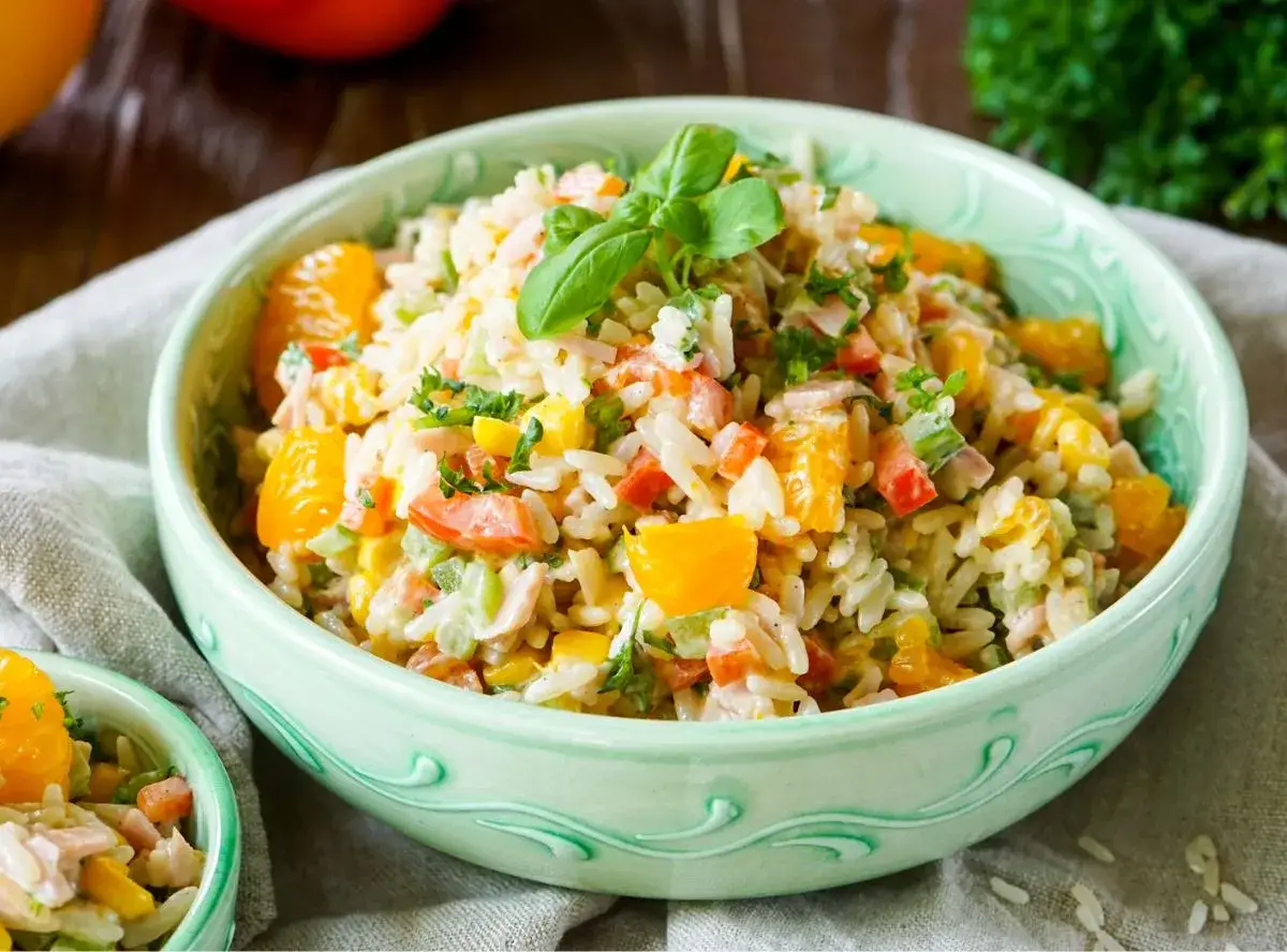 Reissalat mit Mandarinen, Paprika und Kräutern in einer grünen Schüssel, garniert mit Basilikum.