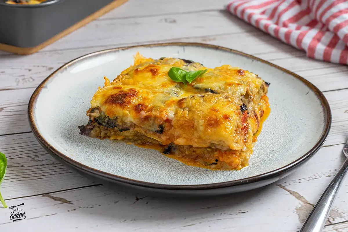 Un trozo de parmigiana di melanzane napoletana, gratinado y con queso derretido, servido en un plato.
