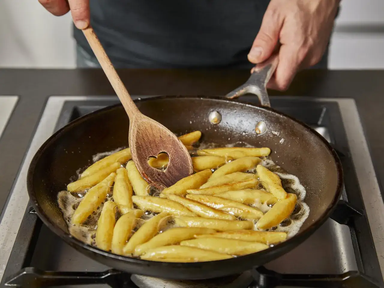 Schupfnudeln werden in einer Pfanne goldbraun gebraten. Ein Kochlöffel mit Herzform rührt die Nudeln für das Schupfnudeln Rezept.