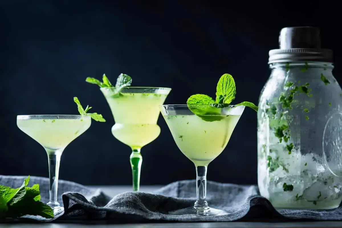 Orzeźwiające mojito z ginem w eleganckich kieliszkach, ozdobione miętą. Obok słoik z lodem i miętą, gotowy do przygotowania kolejnego drinka.