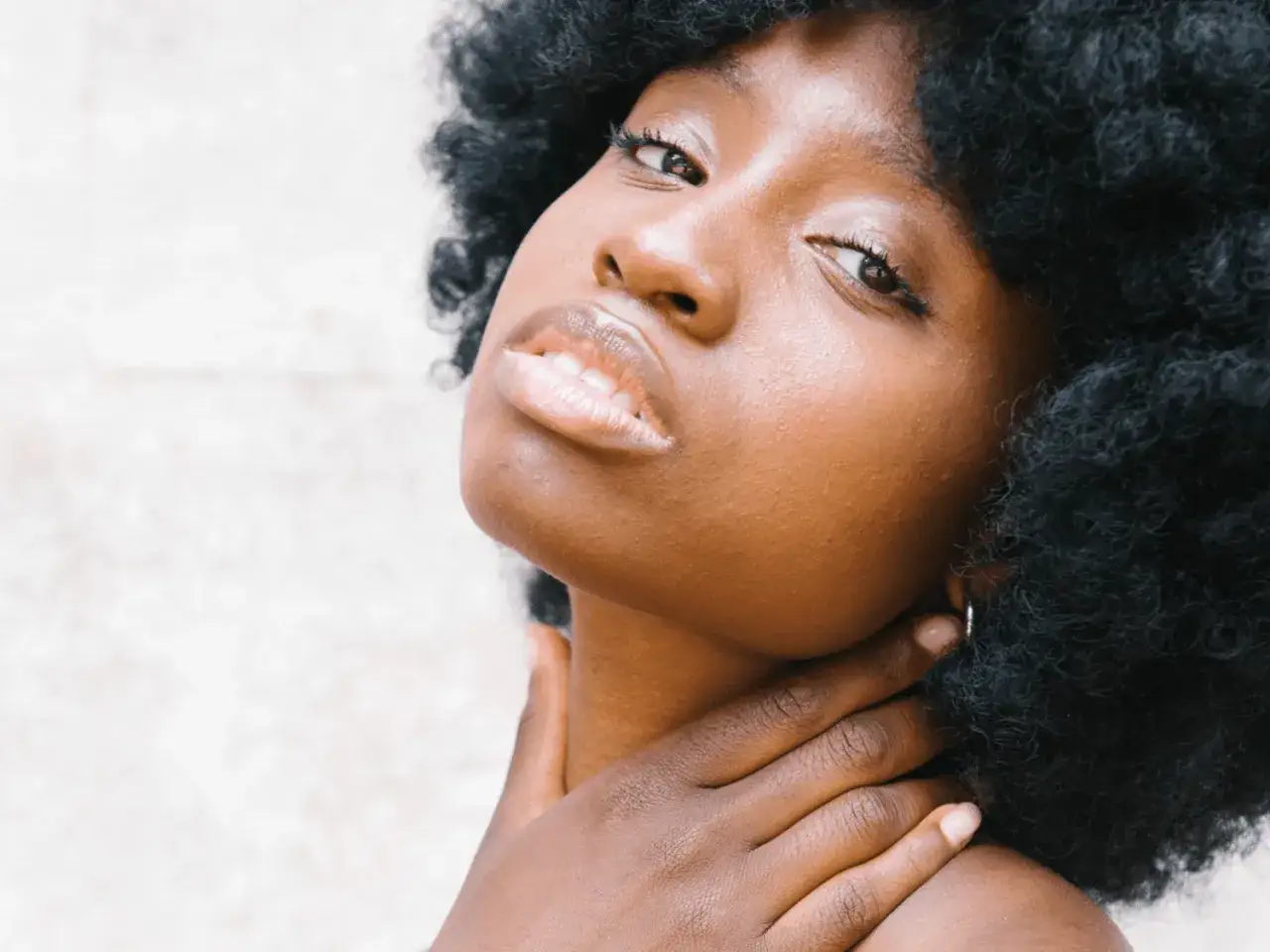 Primo piano di una donna con capelli afro. La sua mano accarezza il collo, un gesto che fa pensare:
