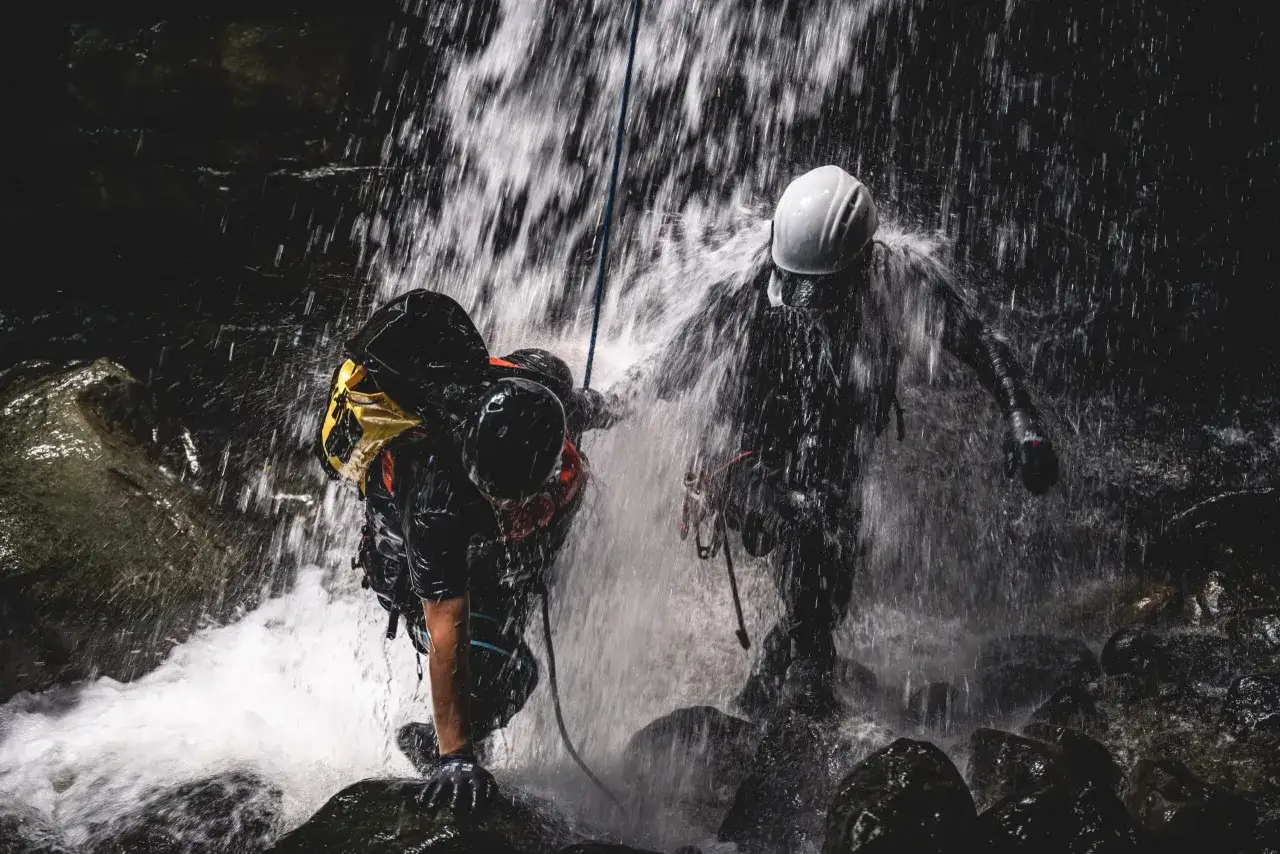 Dw&oacute;ch ludzi w kaskach i sprzęcie zjazdowych pokonuje wodospad. To właśnie jest canyoning &ndash; ekstremalna przygoda w kanionach.