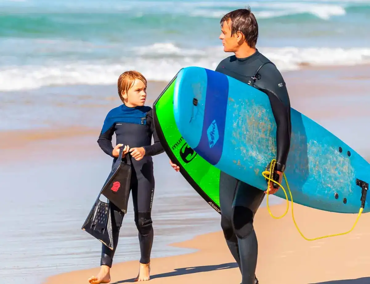 Vater und Sohn mit Surfbrett und Flossen am Strand. Ein perfekter Tag f&uuml;r surfbrett kinder.
