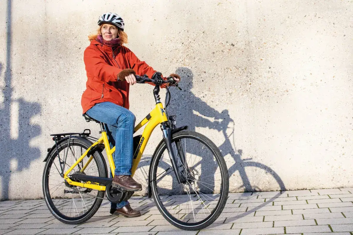Kobieta w kasku i pomarańczowej kurtce siedzi na żółtym rowerze elektrycznym, gotowa do jazdy. Prosty poradnik: jak uruchomić rower elektryczny.