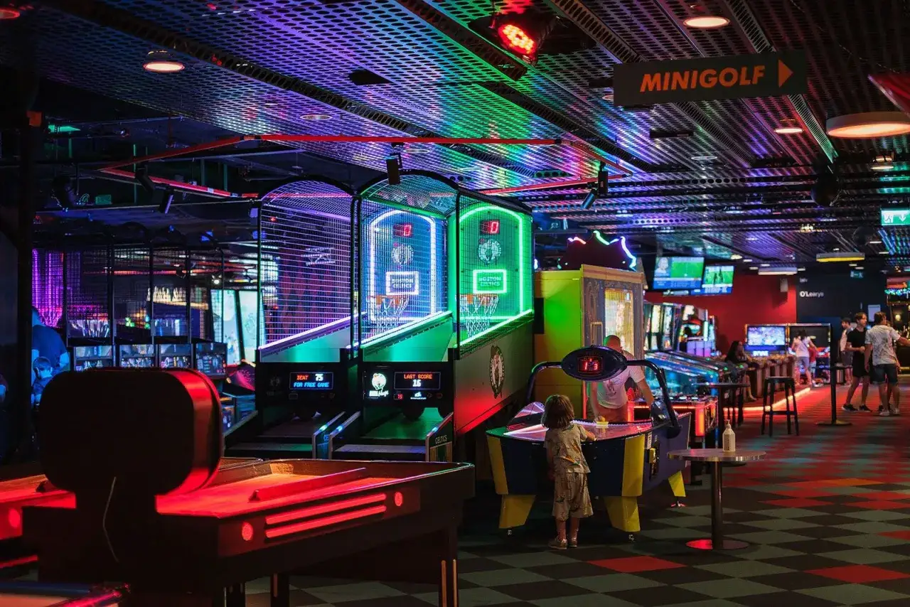 En neonupplyst spelhall med basketspel, airhockey och minigolfskylt. Perfekt för roliga museum i Stockholm.