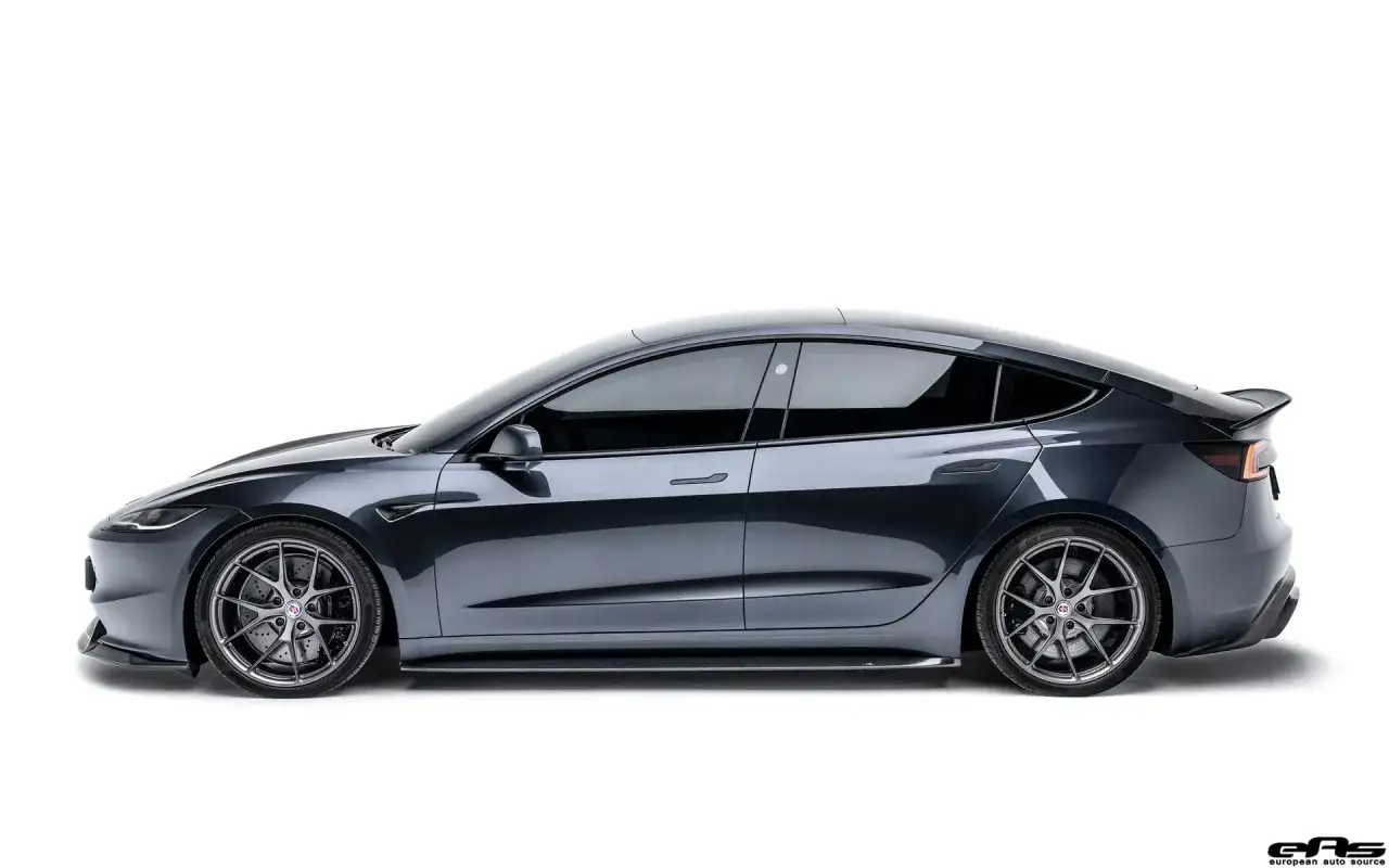 Tesla Model 3 gris oscuro, perfil lateral, llantas deportivas, aler&oacute;n trasero. Un coche el&eacute;ctrico con bajo consumo.