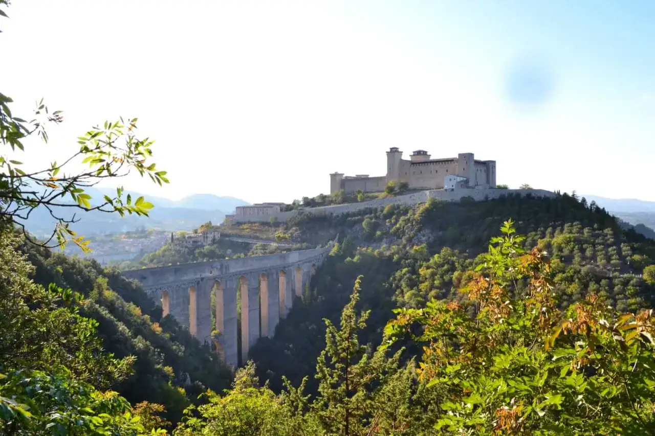 Un imponente castello domina la collina, con un antico acquedotto che attraversa la valle. Un paesaggio suggestivo lungo la via Flaminia.