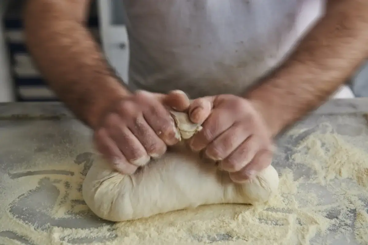 Ręce ugniatają puszyste ciasto na pizzę, obsypane mąką.