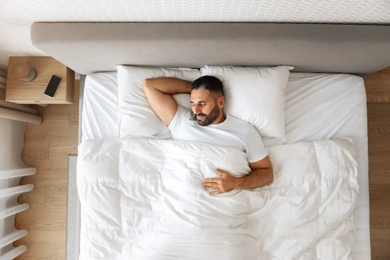 Hombre durmiendo pl&aacute;cidamente en una cama blanca. Un ejemplo de c&oacute;mo dormir bien, sin distracciones.