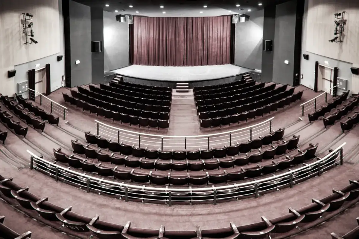 Pusta sala widowni w teatrze im. Aleksandra Sewruka w Elblągu, z rzędami czerwonych foteli i sceną z zasłoną.
