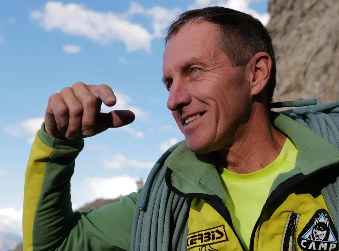 Denis Urubko, alpiniste expérimenté, sourit sous un ciel bleu, une corde d'escalade autour du cou.