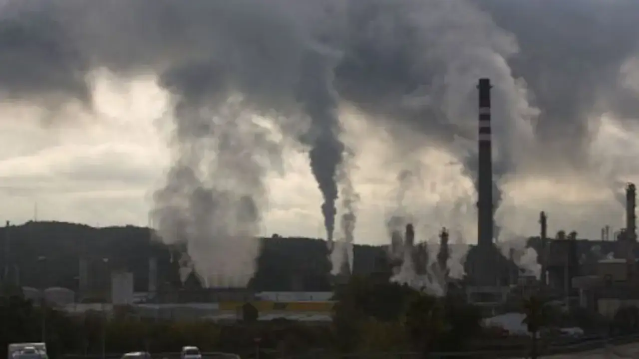 Chimeneas industriales emiten humo denso, creando una atmósfera sombría. Parece la escena de la ciudad más contaminada del mundo.