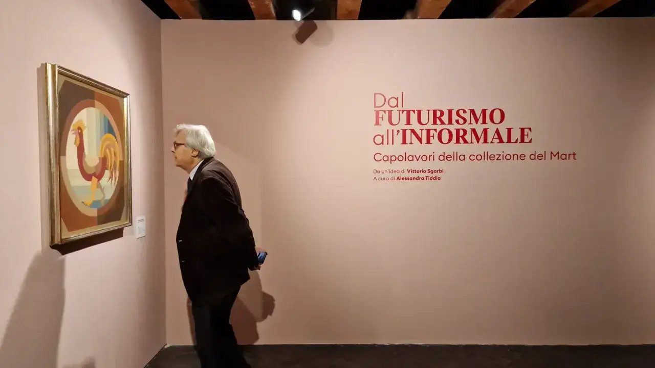 Un uomo osserva un quadro di un gallo in una delle mostre di Ancona. L'esposizione 
